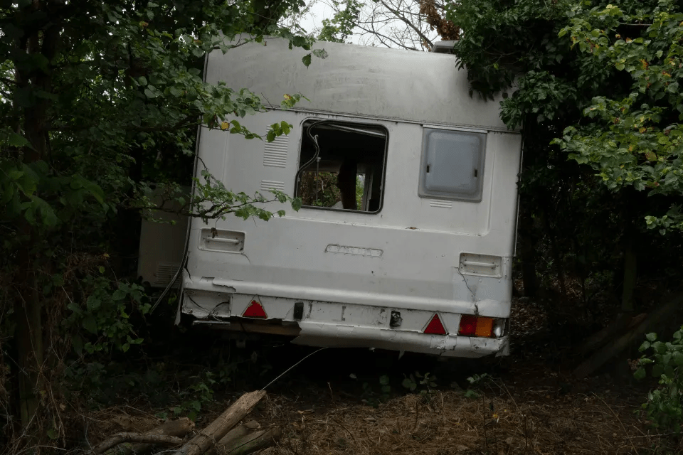a white camper with a broken window is stuck in the woods