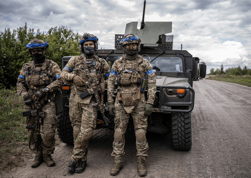 three soldiers stand in front of a military vehicle