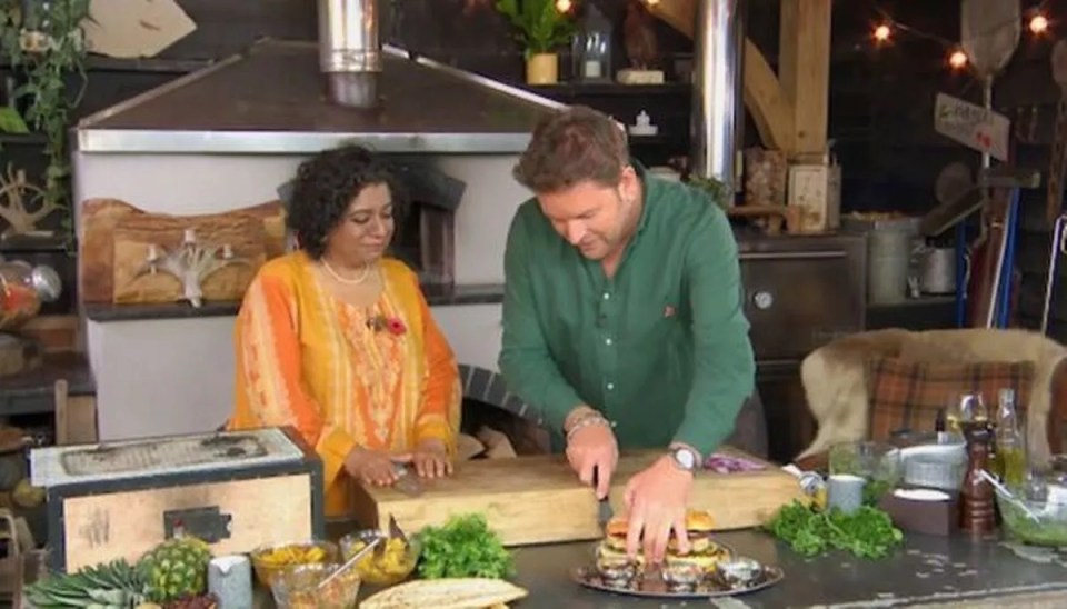 a man is cutting a hamburger on a cutting board while a woman watches .