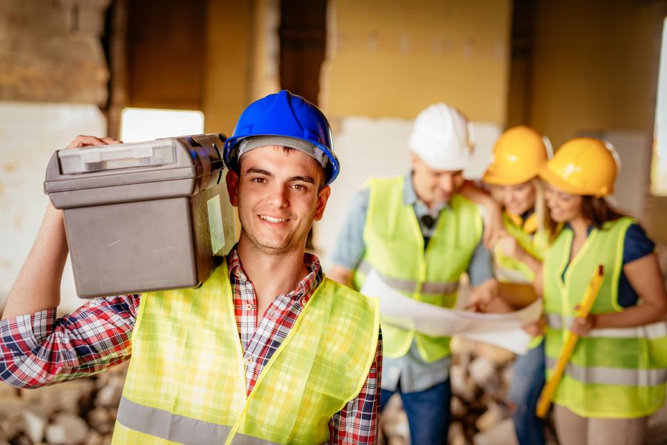 a man wearing a hard hat is carrying a toolbox