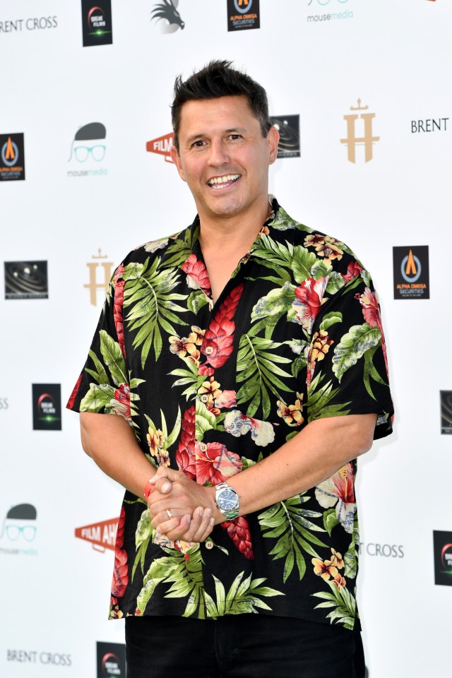a man in a hawaiian shirt stands in front of a brent cross sign