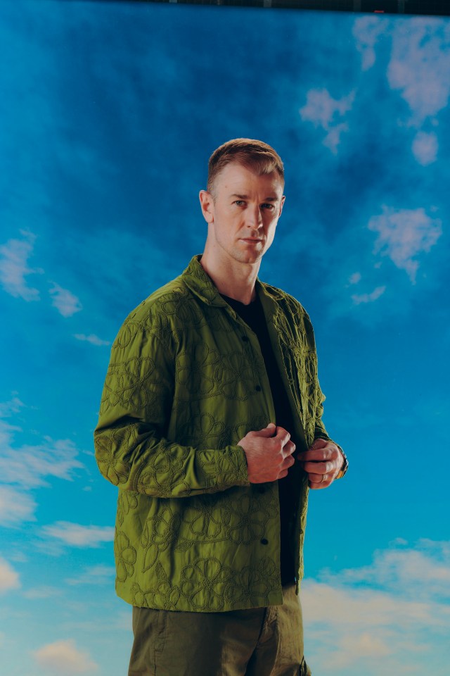 a man in a green jacket stands in front of a blue sky