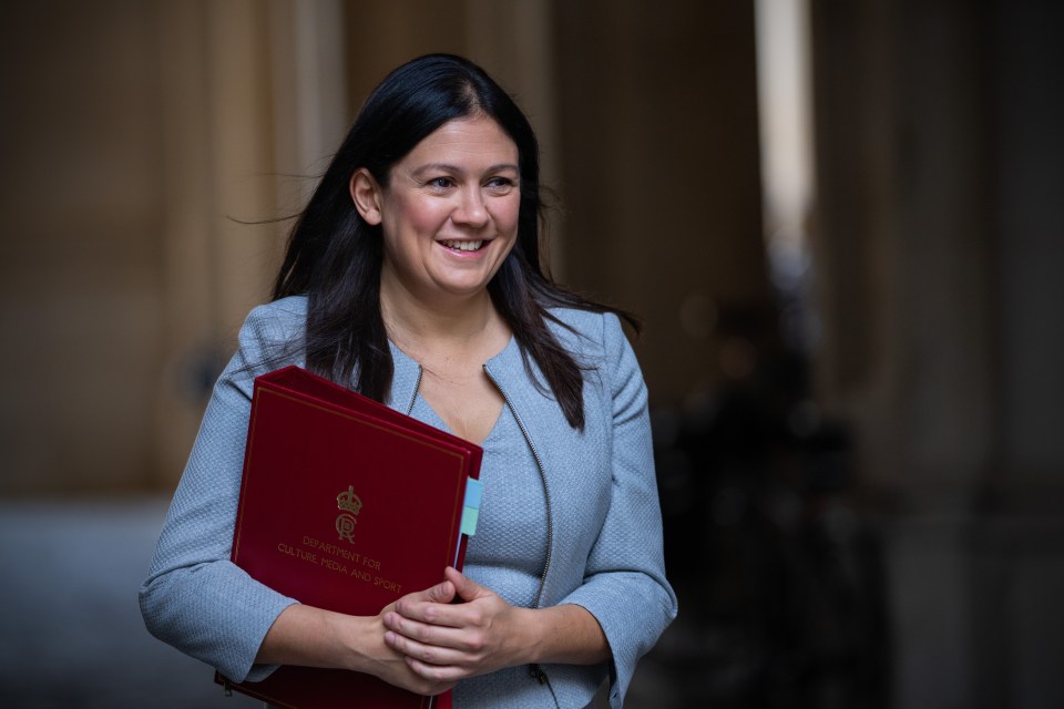a woman in a grey jacket holds a red folder that says ' secretary of state ' on it