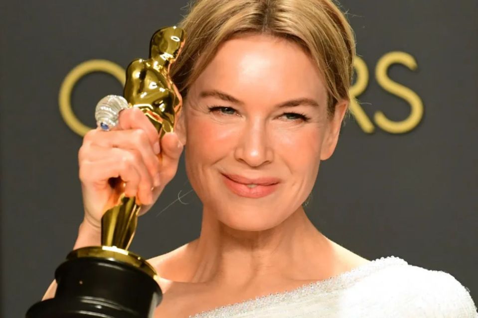 a woman holds an oscar statue in front of a sign that says oscars