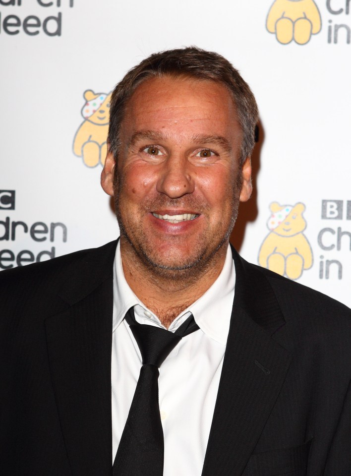 a man in a suit and tie smiles in front of a sign that says bbc children in need
