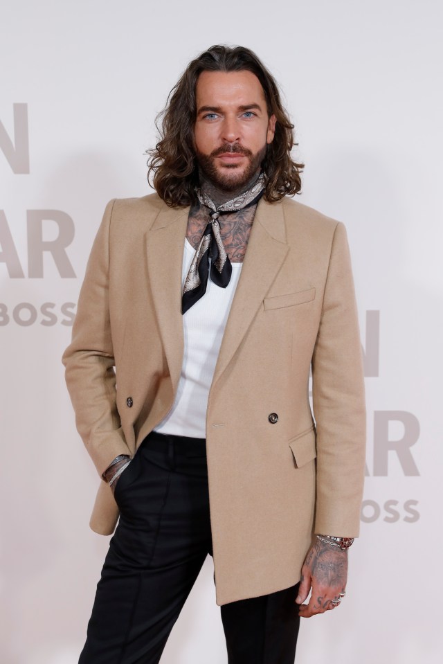 a man with long hair and a scarf around his neck stands in front of a wall that says boss