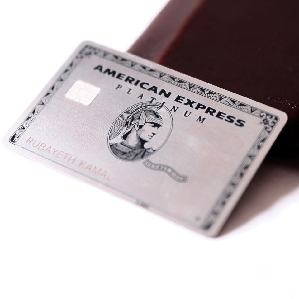 a silver american express platinum card sits on top of a brown wallet