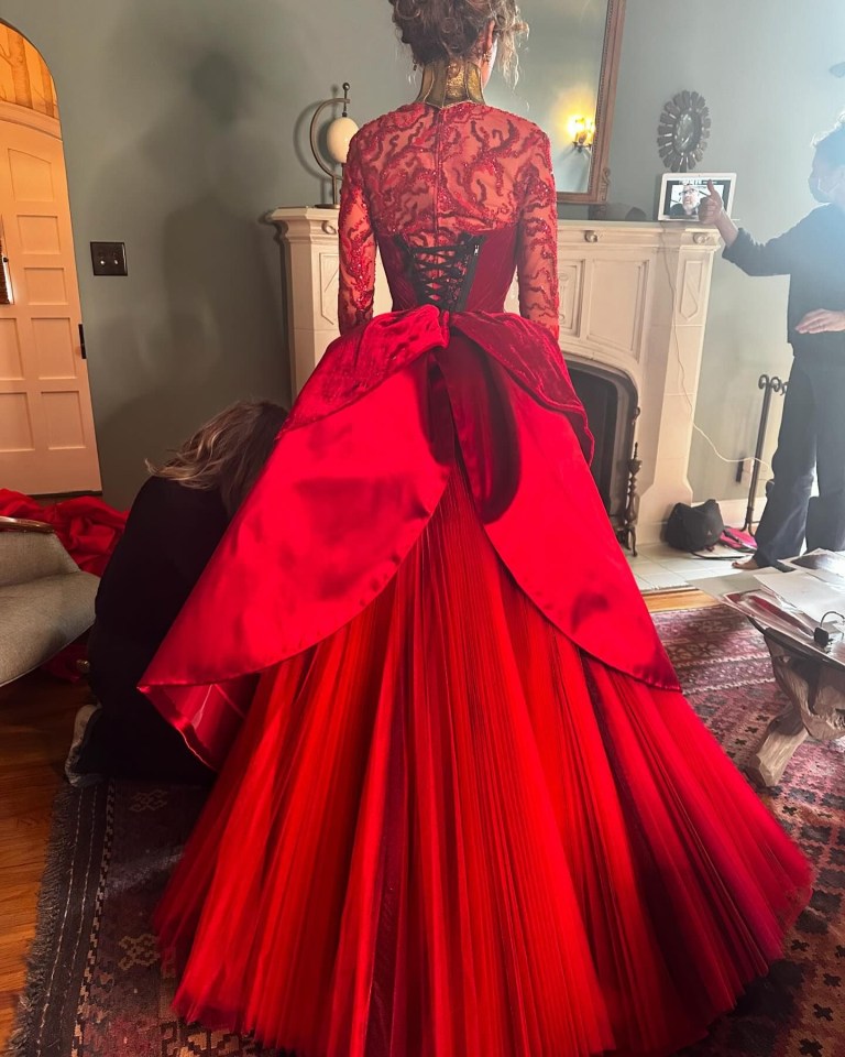 a woman in a red dress is standing in front of a fireplace
