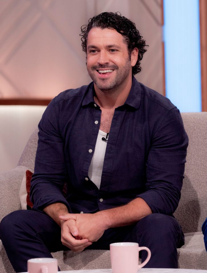 a man in a blue shirt sits on a couch smiling