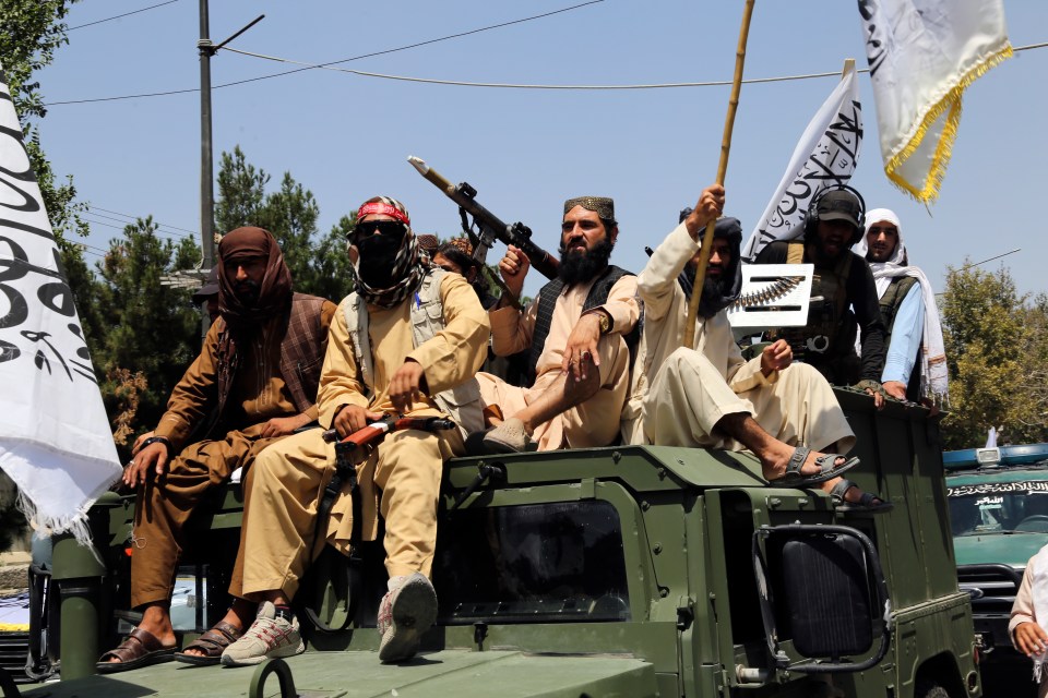 a group of men are sitting on top of a military vehicle holding flags