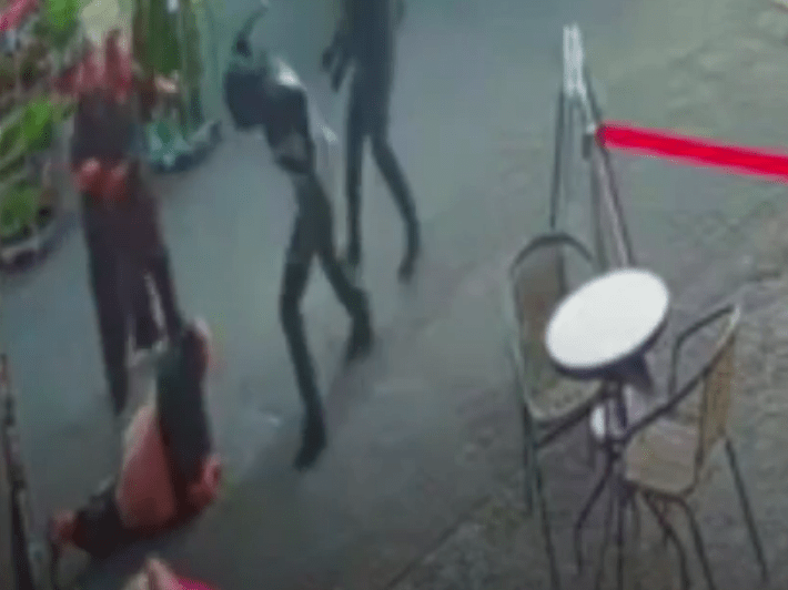 a group of people are standing around a table and chairs on a sidewalk .