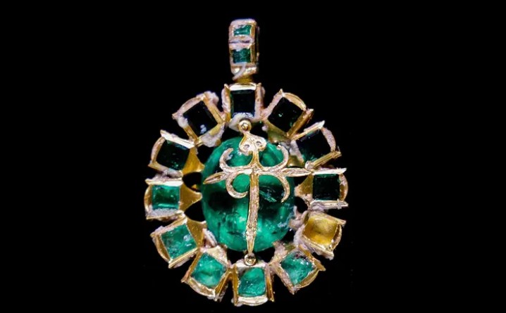 a gold pendant with emeralds and diamonds on a black background