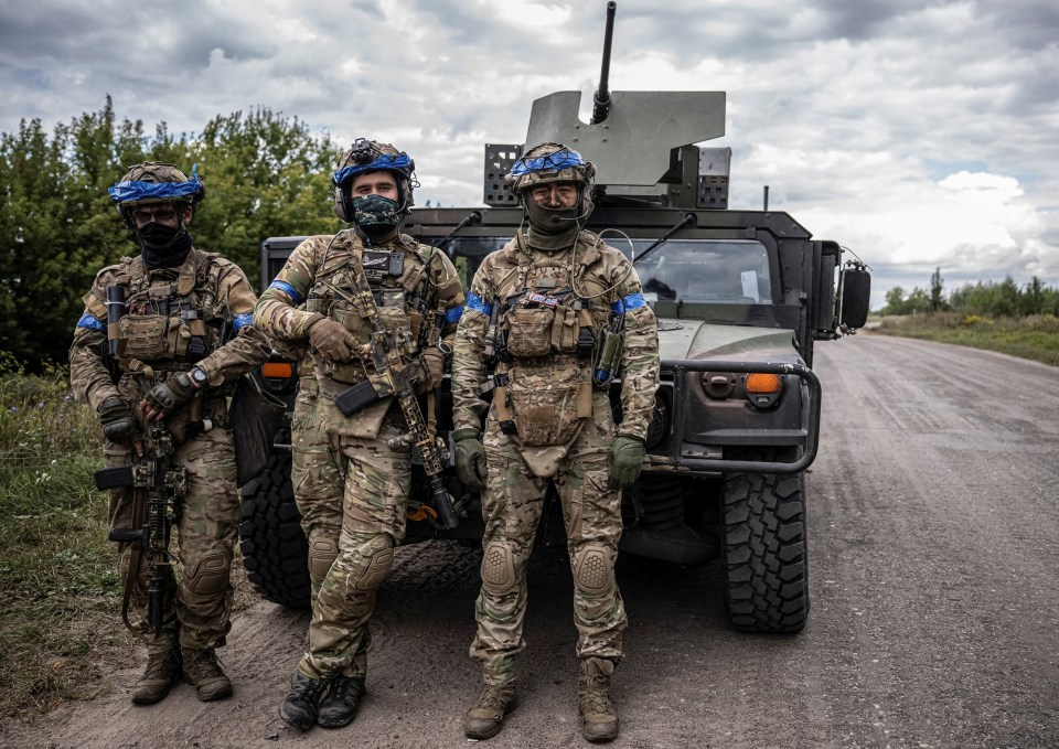 three soldiers stand in front of a military vehicle