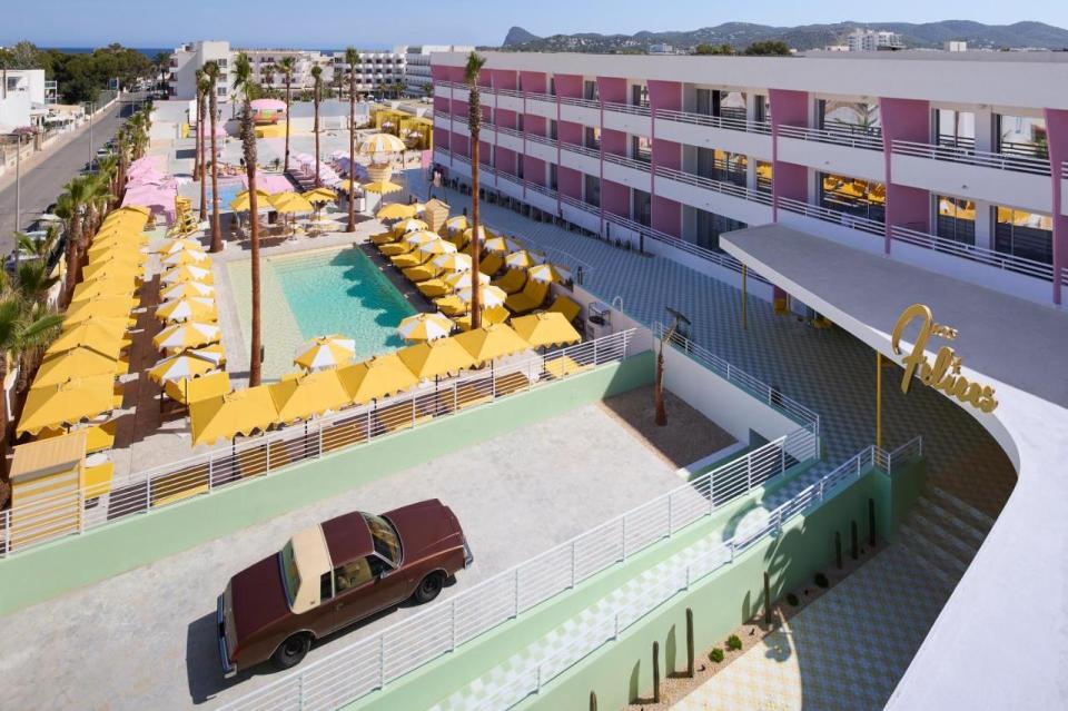 a car is parked in front of a hotel with a pool and umbrellas