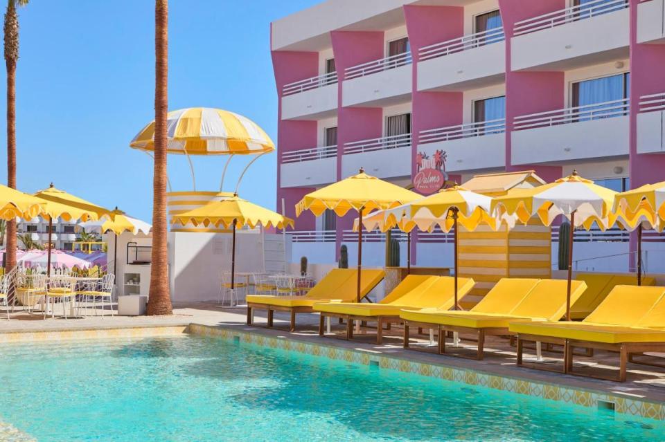 a pool with yellow chairs and umbrellas in front of a building that says palm springs