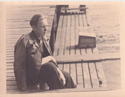 a black and white photo of a man sitting on a dock