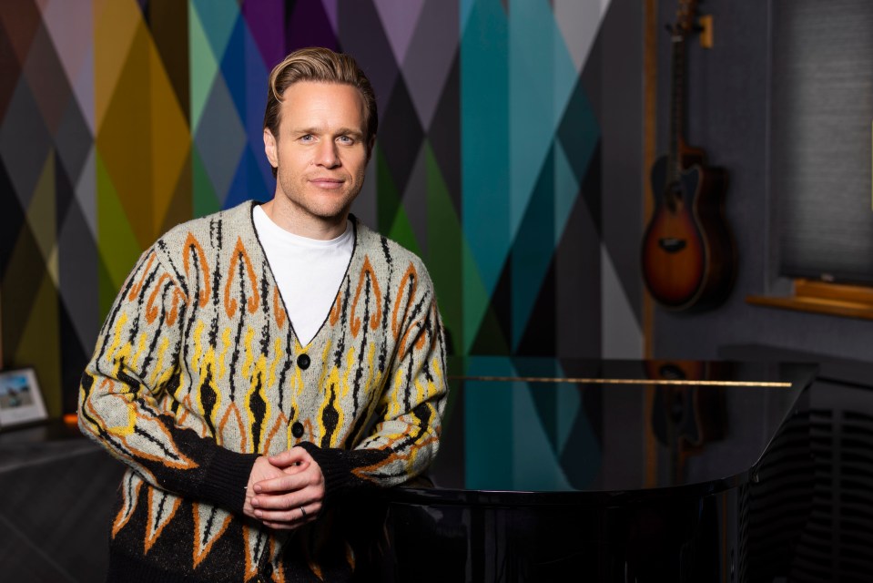a man in a colorful sweater stands in front of a piano