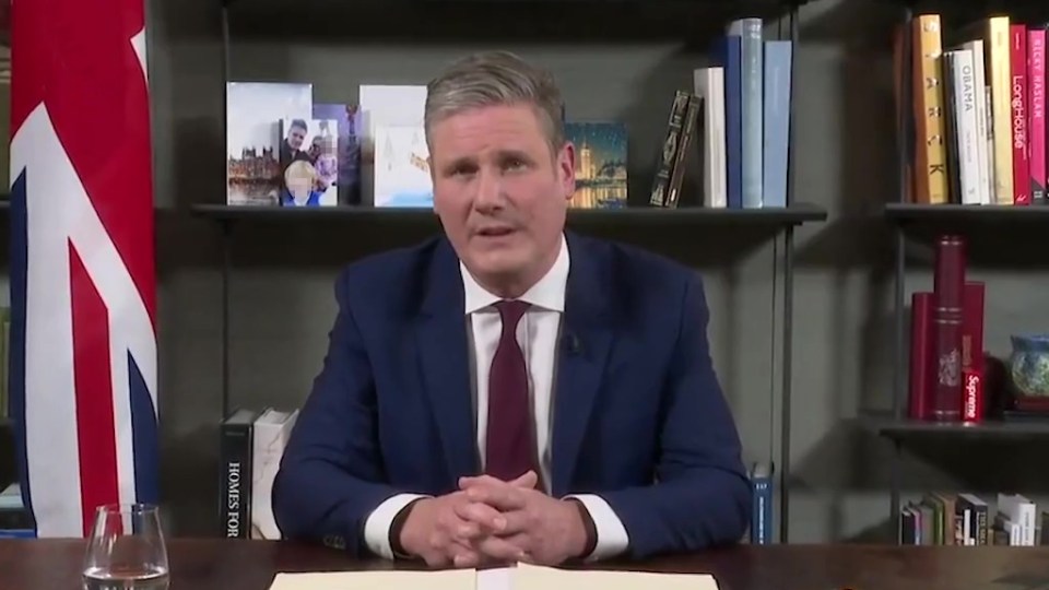 a man in a suit and tie sits at a desk in front of a bookshelf that says supreme