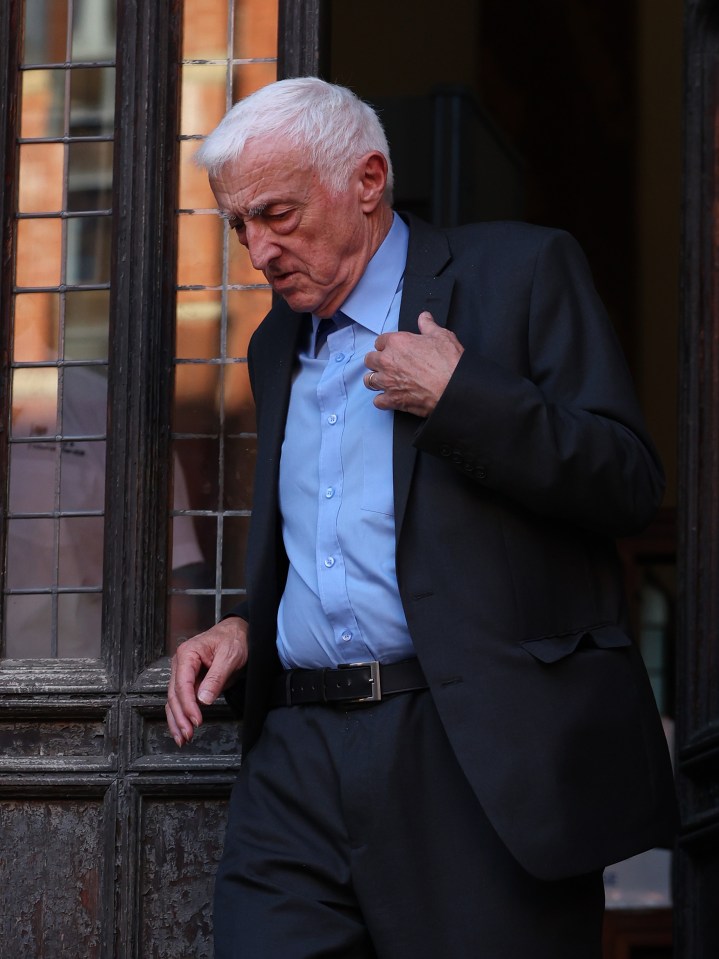 a man in a suit and blue shirt is standing in front of a window