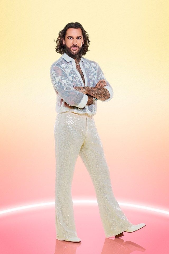 a man in a white shirt and white sequined pants stands with his arms crossed