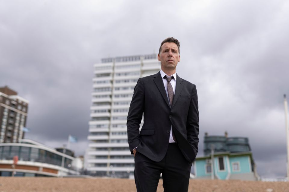 a man in a suit and tie stands with his hands in his pockets
