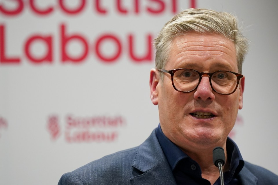 a man wearing glasses stands in front of a sign that says scottish labour