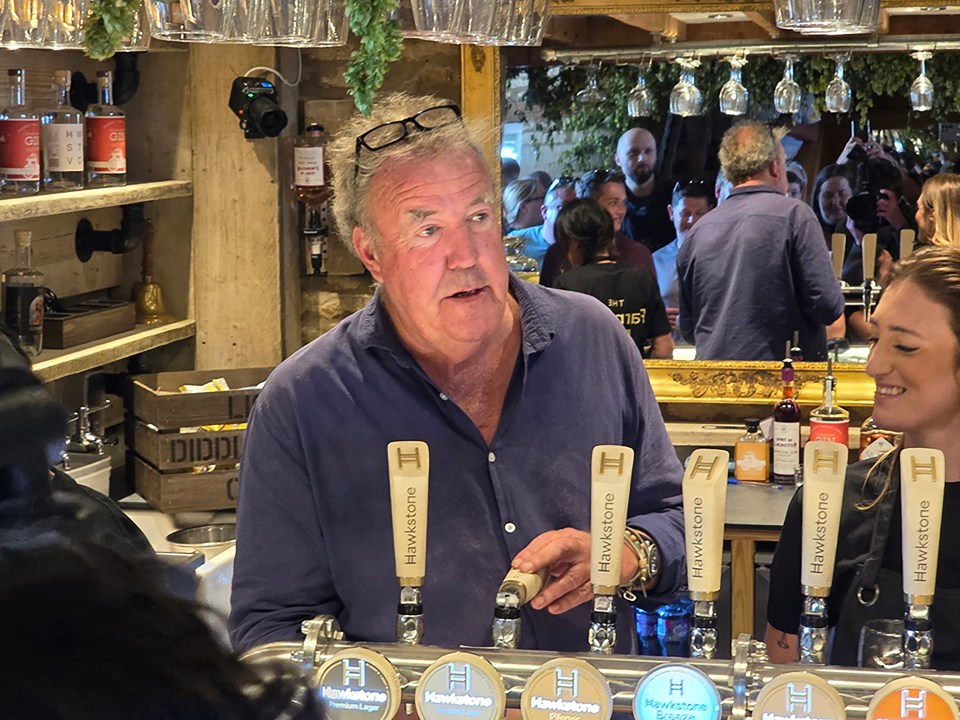 a man stands behind a bar with hawkstone beer taps