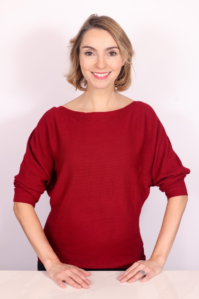 a woman in a red sweater smiles with her hands on her hips
