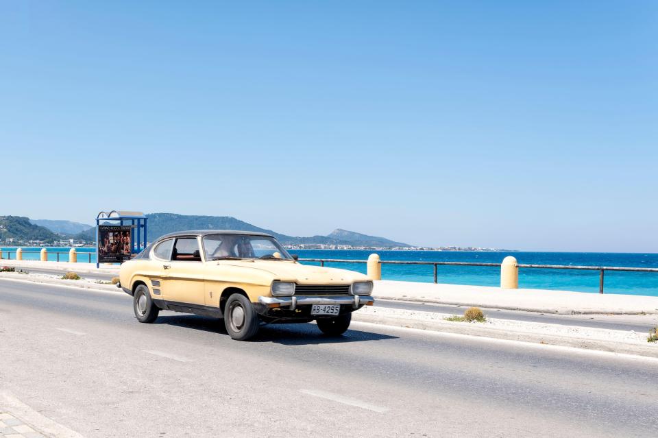 a yellow car is driving down a road near the ocean