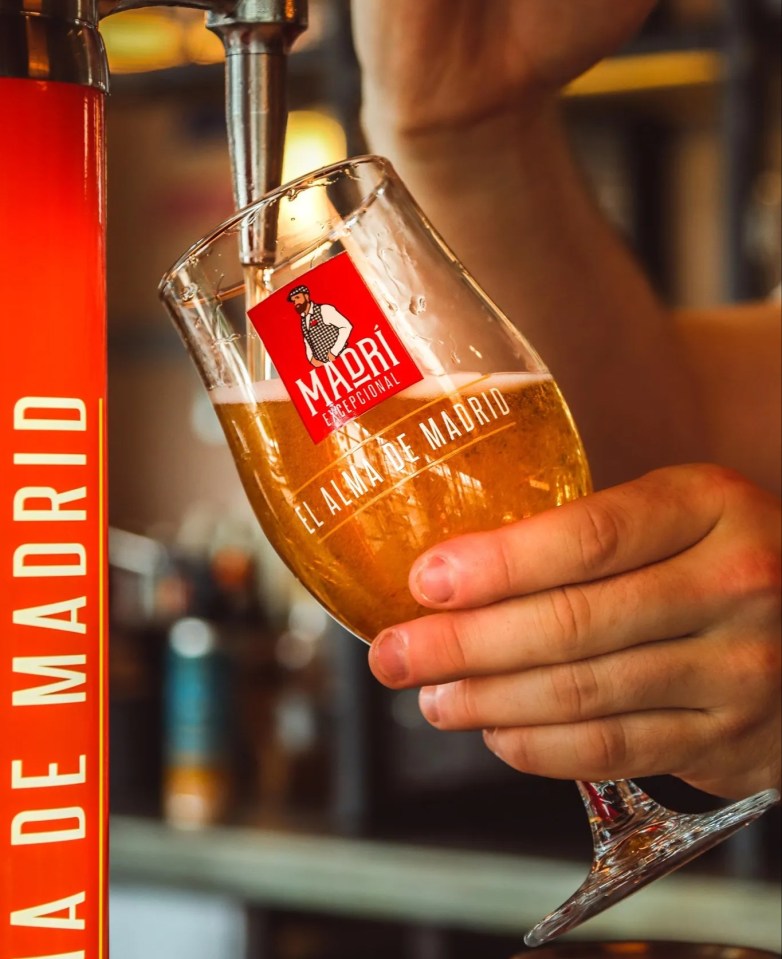 a person pouring beer into a glass that says madri on it