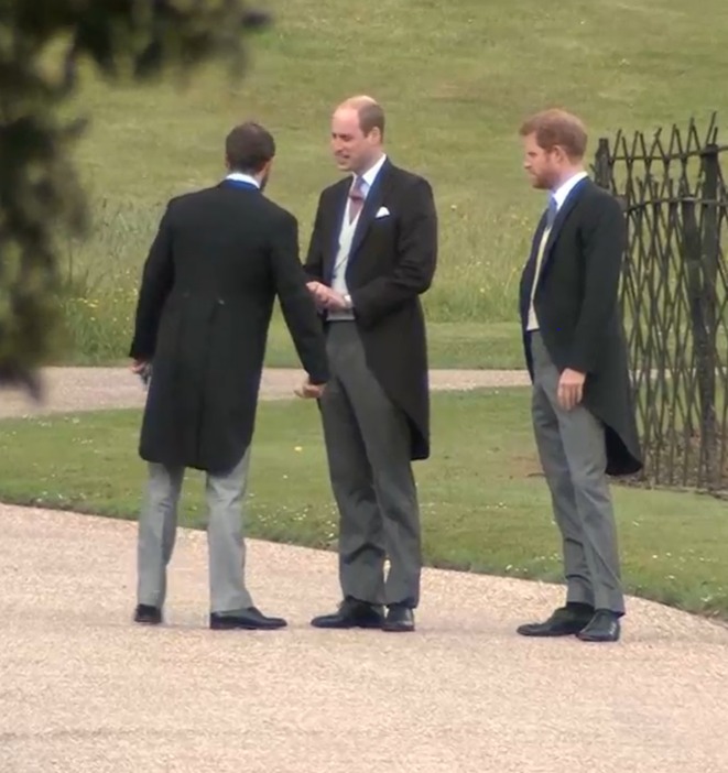 three men in suits are standing on a gravel path talking to each other