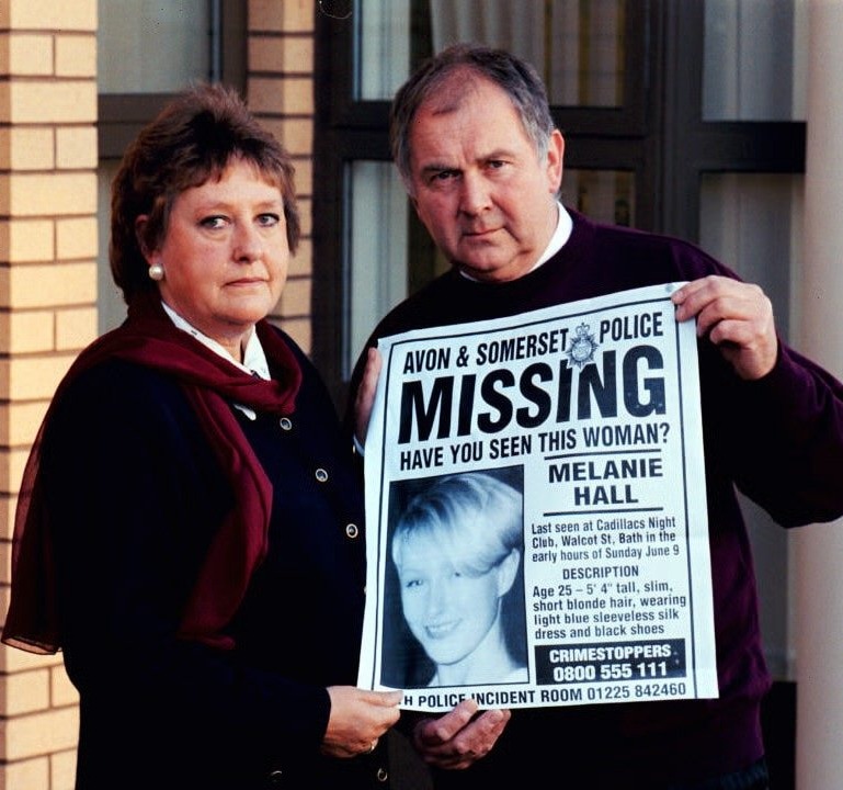 a man and woman holding a poster that says avon & somerset police missing melanie hall