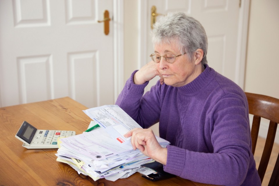 BK3AMD Elderly senior woman pensioner OAP lady retiree with a big pile of bills on the table looking depressed at a large gas fuel bill. UK Britain