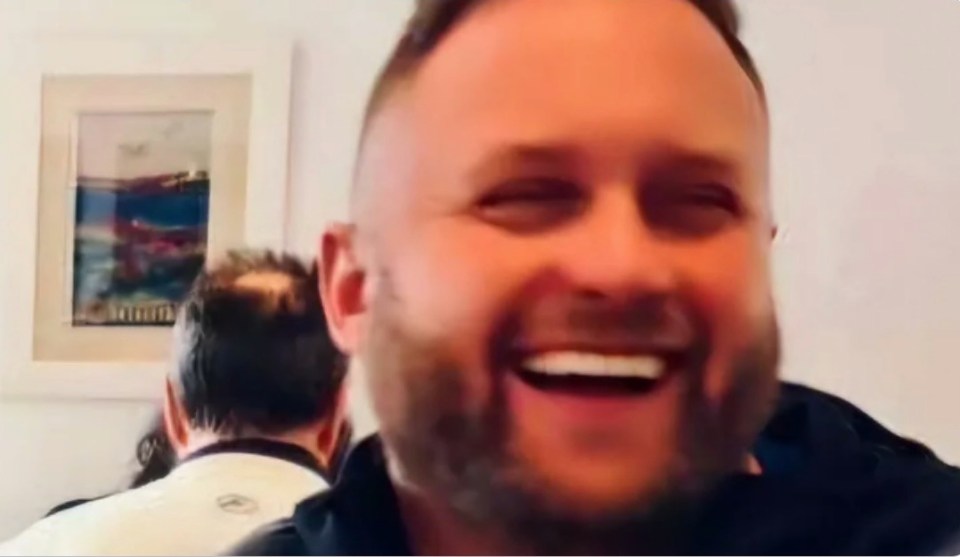 a man with a beard is laughing with another man in the background .