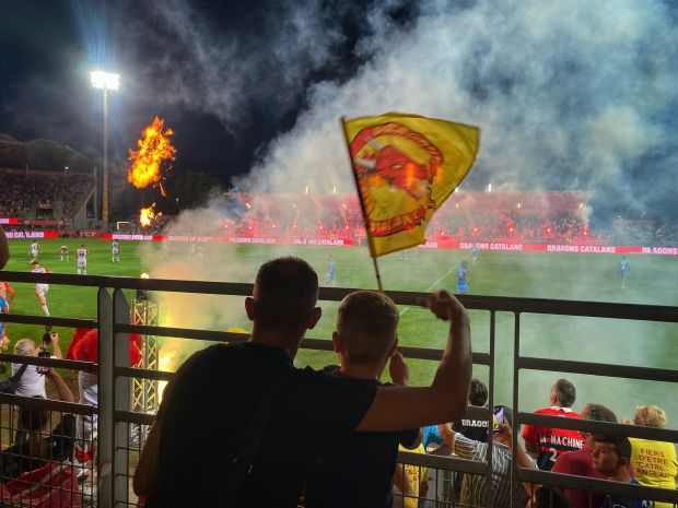 a man holding a flag in front of a soccer field that says dragons catalans