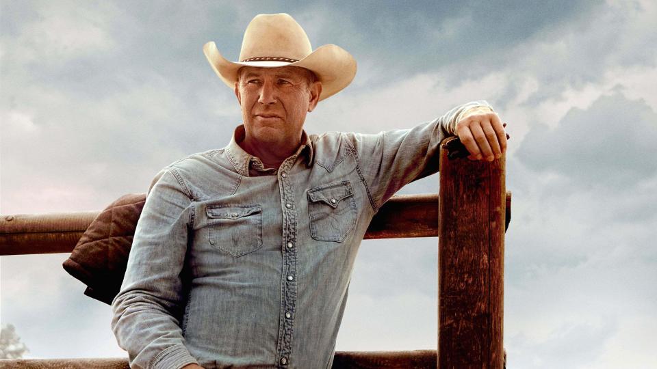 a man in a cowboy hat leans against a wooden fence post