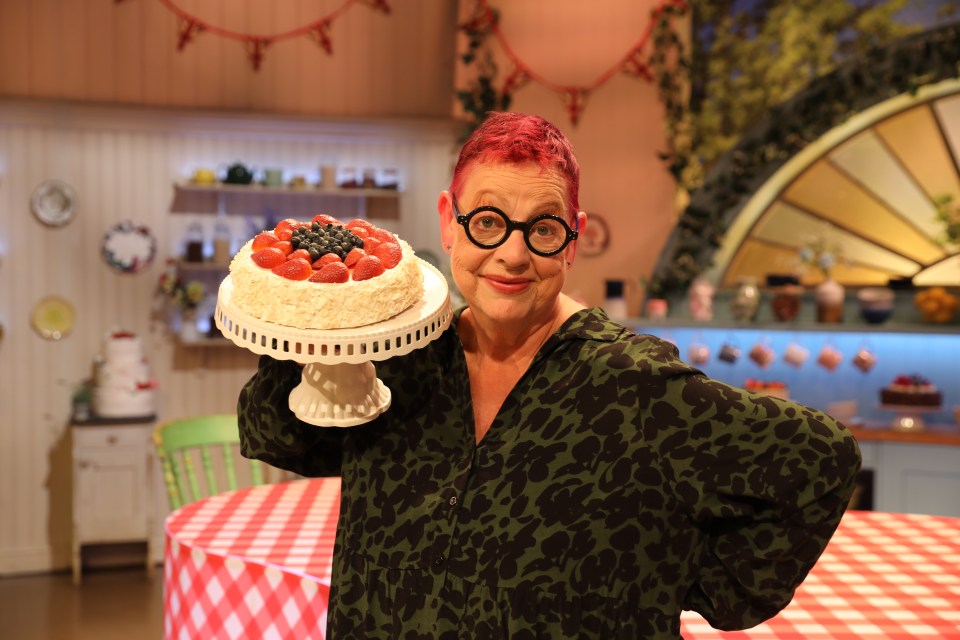 a woman holding a cake with strawberries and blueberries on top