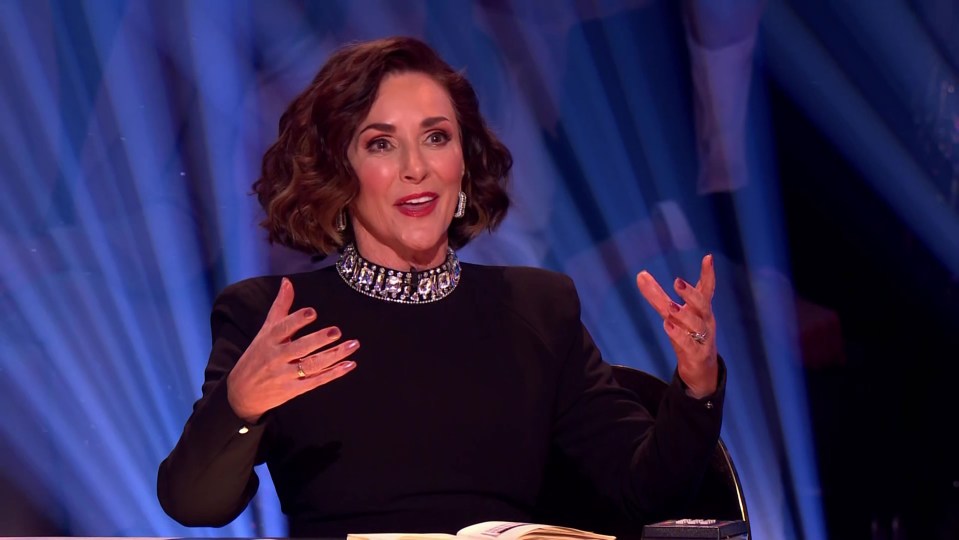 a woman in a black dress is sitting at a table with her hands outstretched