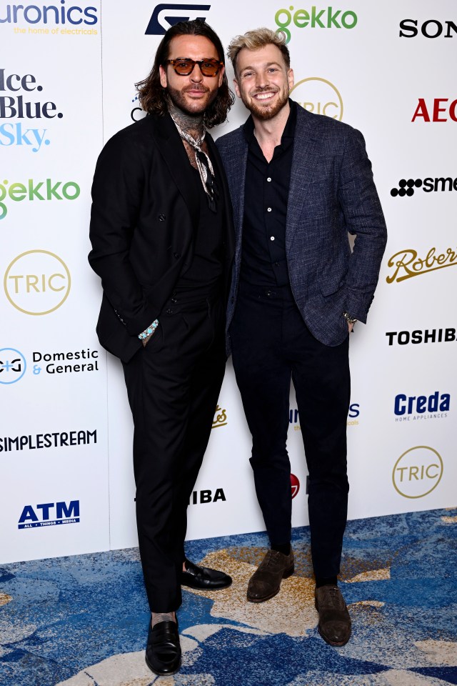 two men are posing for a picture in front of a wall that says tric
