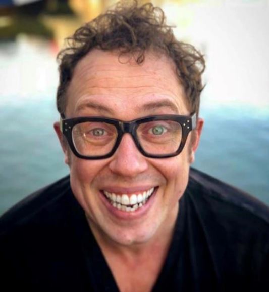 a man wearing glasses and a black shirt is smiling for the camera .