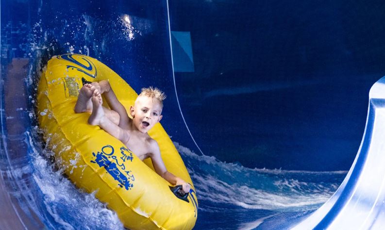 a young boy is riding down a water slide on a tube that says ocean splash