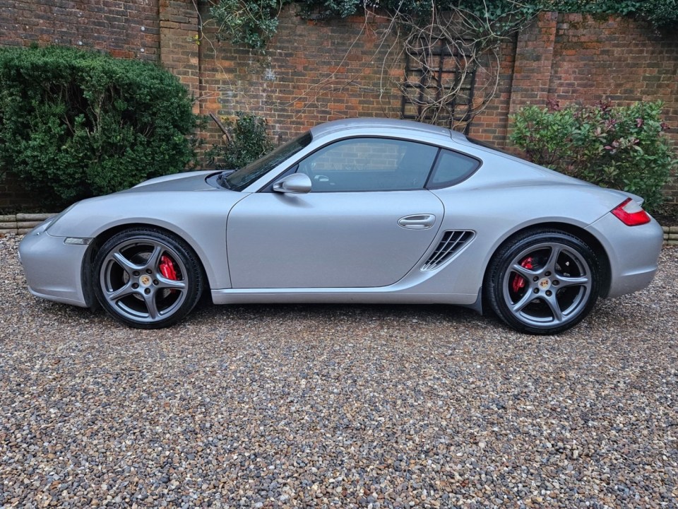 a silver sports car is parked on gravel in front of a brick wall