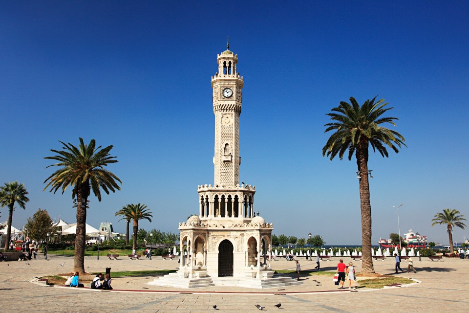 a clock tower surrounded by palm trees and people