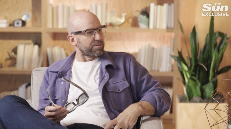 a man wearing glasses sits in a chair with the sun exclusive written on the bottom