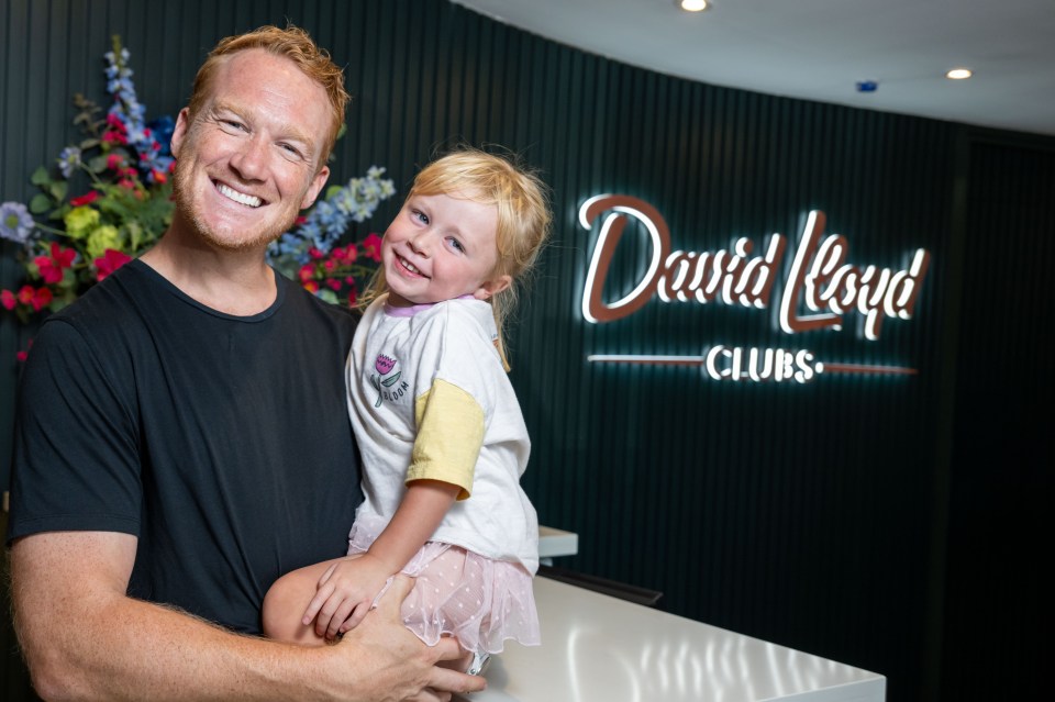 a man holds a little girl in front of a david lloyd clubs sign