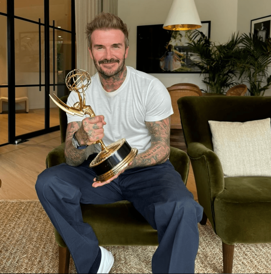 a man is sitting in a chair holding an emmy award