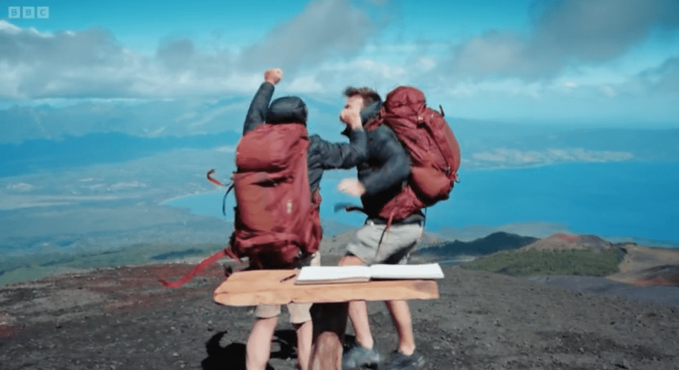 two men with backpacks standing on top of a mountain