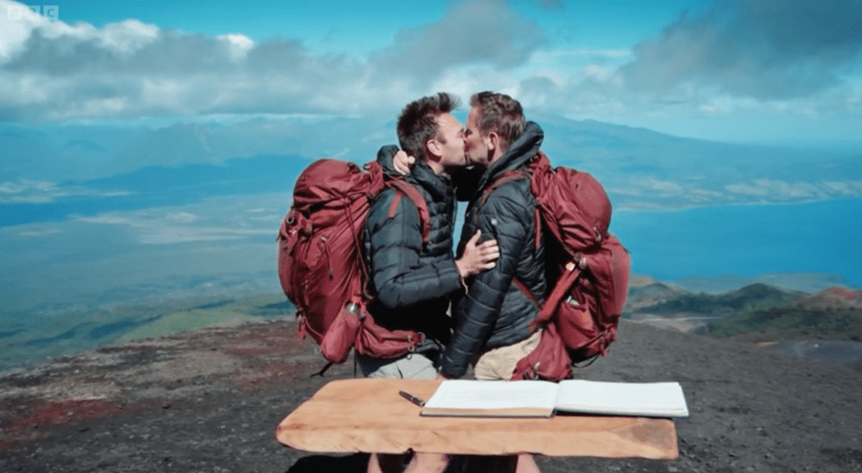 two men kissing on top of a mountain with a bbc logo in the background