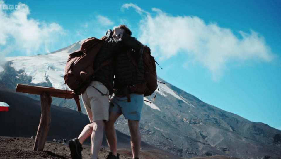 two people with backpacks looking at a mountain with bbc on the bottom right