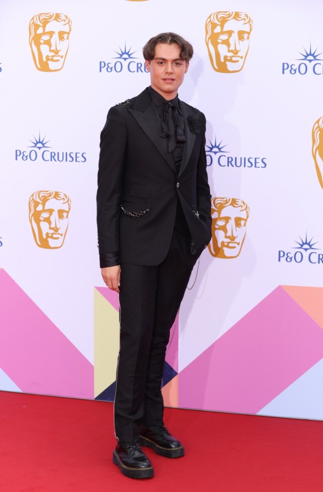 a man in a black suit stands on a red carpet in front of a p & o cruises sign